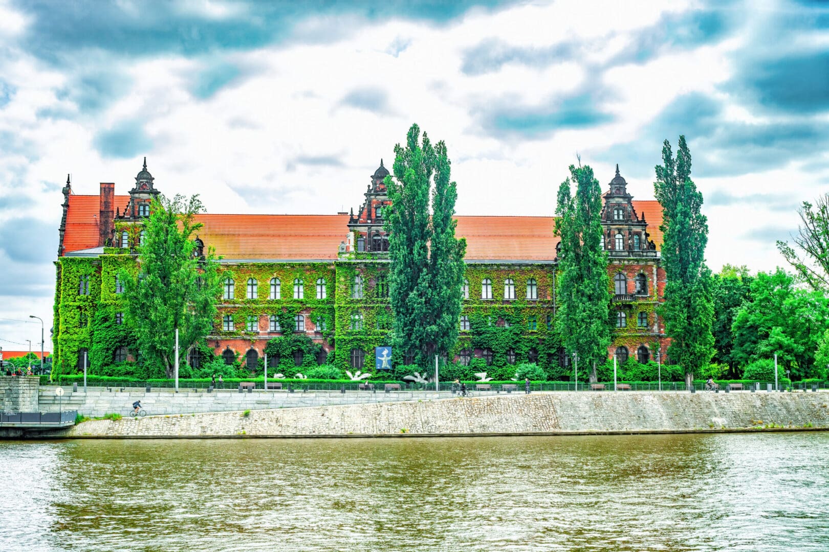 Wroclaw, Poland - 25 May 2023: Wroclaw National Museum, view from Oder river. Summer landscape with overgrown historical building and Odra river in Lower Silesia