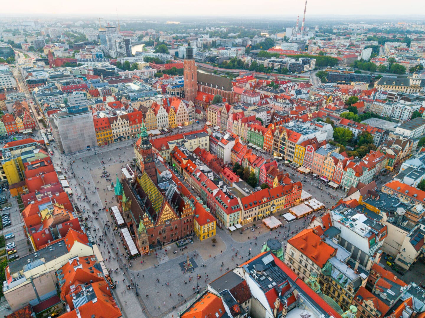 Drone panorama of Wrocław Market Square, one of the largest medieval squares in Europe, surrounded by colorful townhouses and historic Gothic architecture. The Old Town features the Wrocław Town Hall with its ornate facade, bustling streets, cafes, and crowds of tourists. A vibrant cultural and architectural landmark in Lower Silesia, Poland.